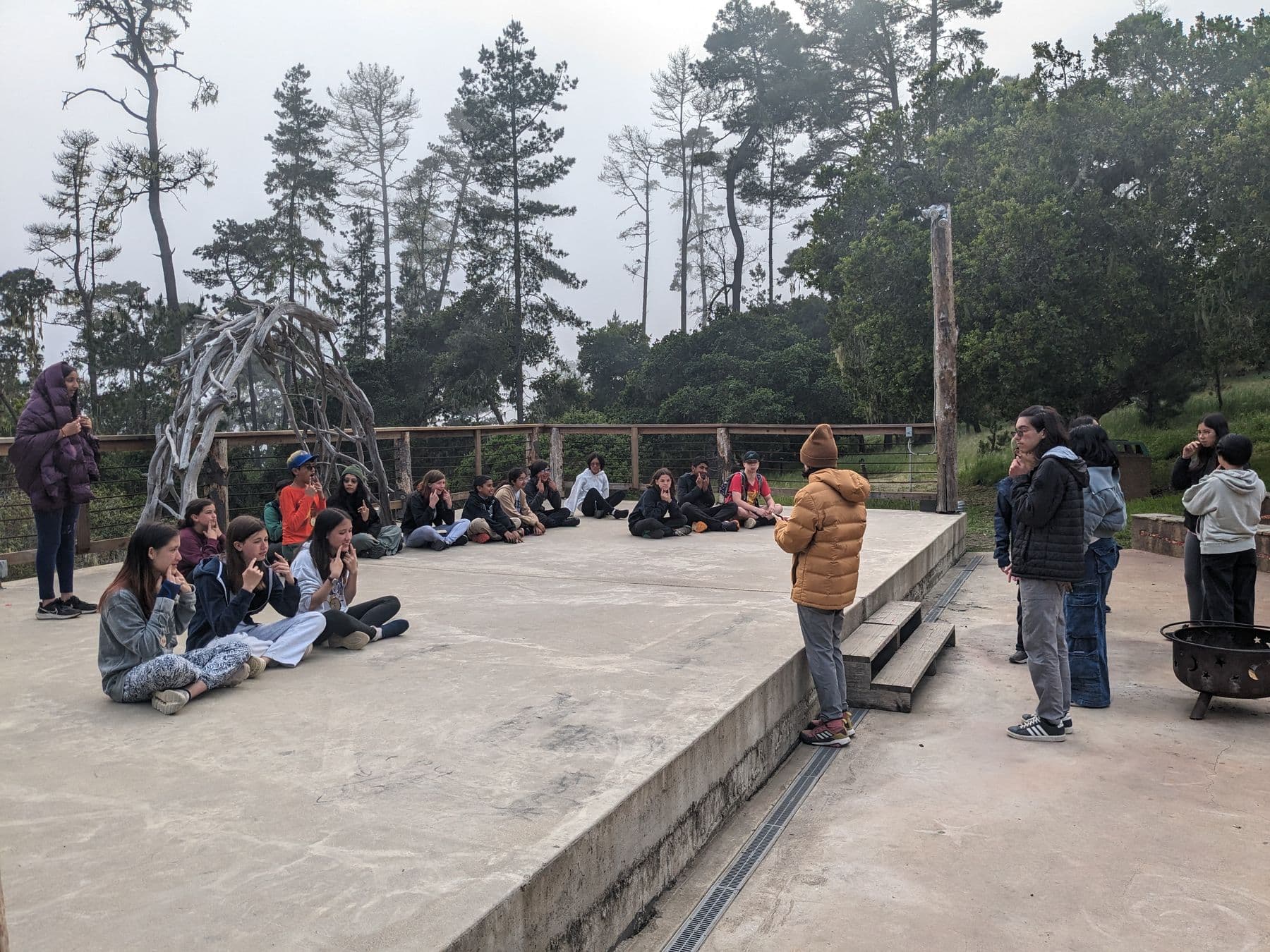 Middle school students gathered on an outdoor stage among the trees